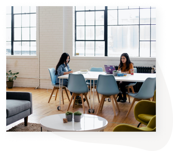 Two women work as a communal table, notebooks and laptops on display.