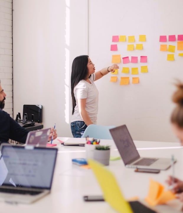 A woman stands before notes she's made that are displayed on the wall during a work meeting.